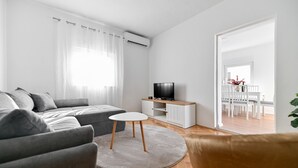 Ein modernes Wohnzimmer mit einem grauen Sofa, einem kleinen weißen Tisch und einem Fernseher auf einem weißen Schrank.