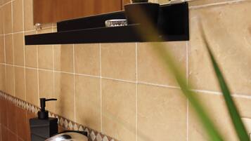 Un bagno con un lavandino bianco, un rubinetto cromato e un dispenser per sapone nero. Sopra il lavandino è presente un armadietto in legno e uno specchio con un asciugamano appeso alla porta.