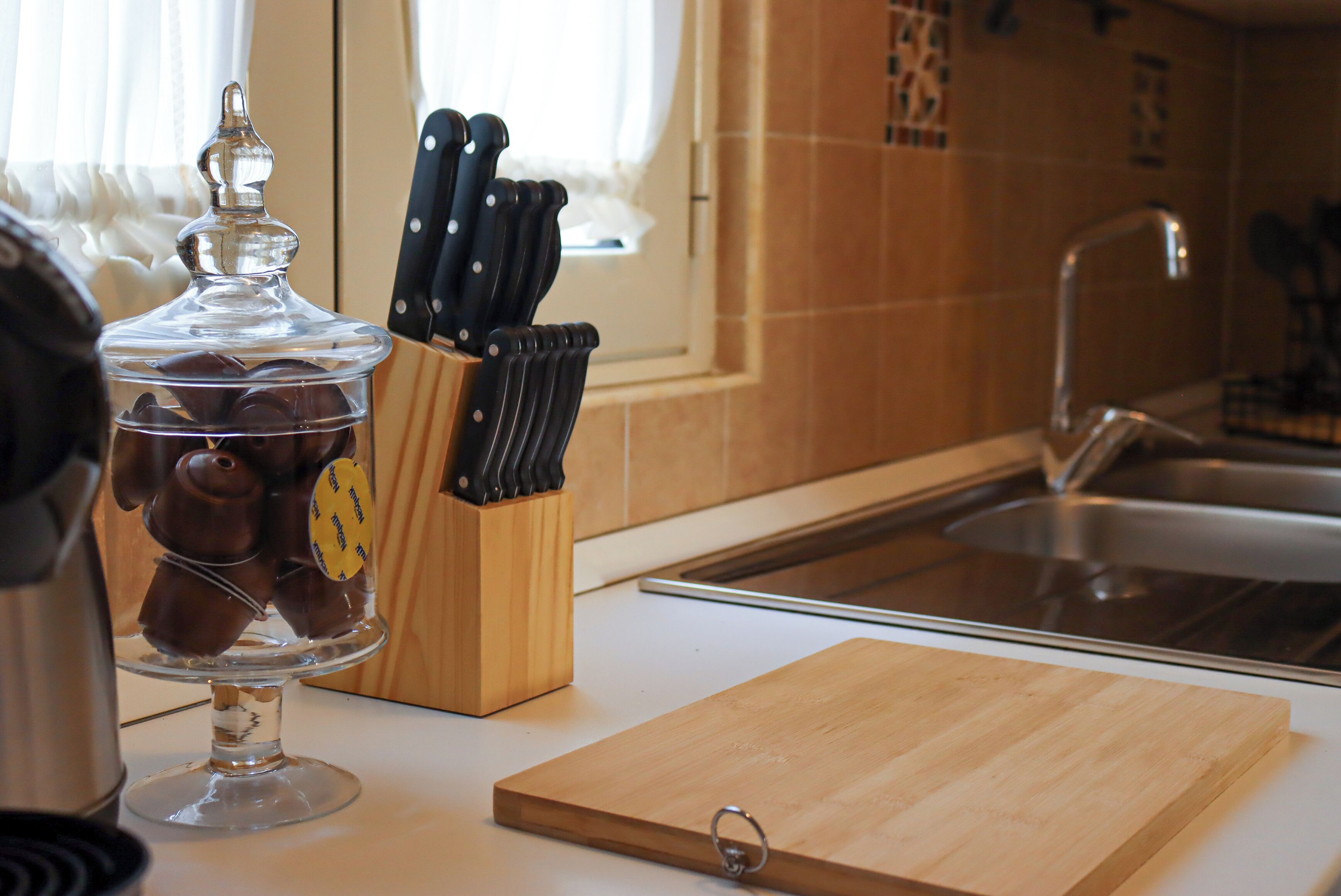 Uma bancada de cozinha com um pote de vidro cheio de chocolates, um bloco de facas de madeira e uma tábua de corte.