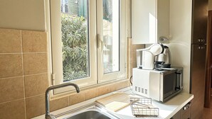 A kitchen with a stainless steel sink, a window with a view of greenery, a microwave, and a kettle. - All'Ombra Della Reggia (Caserta)