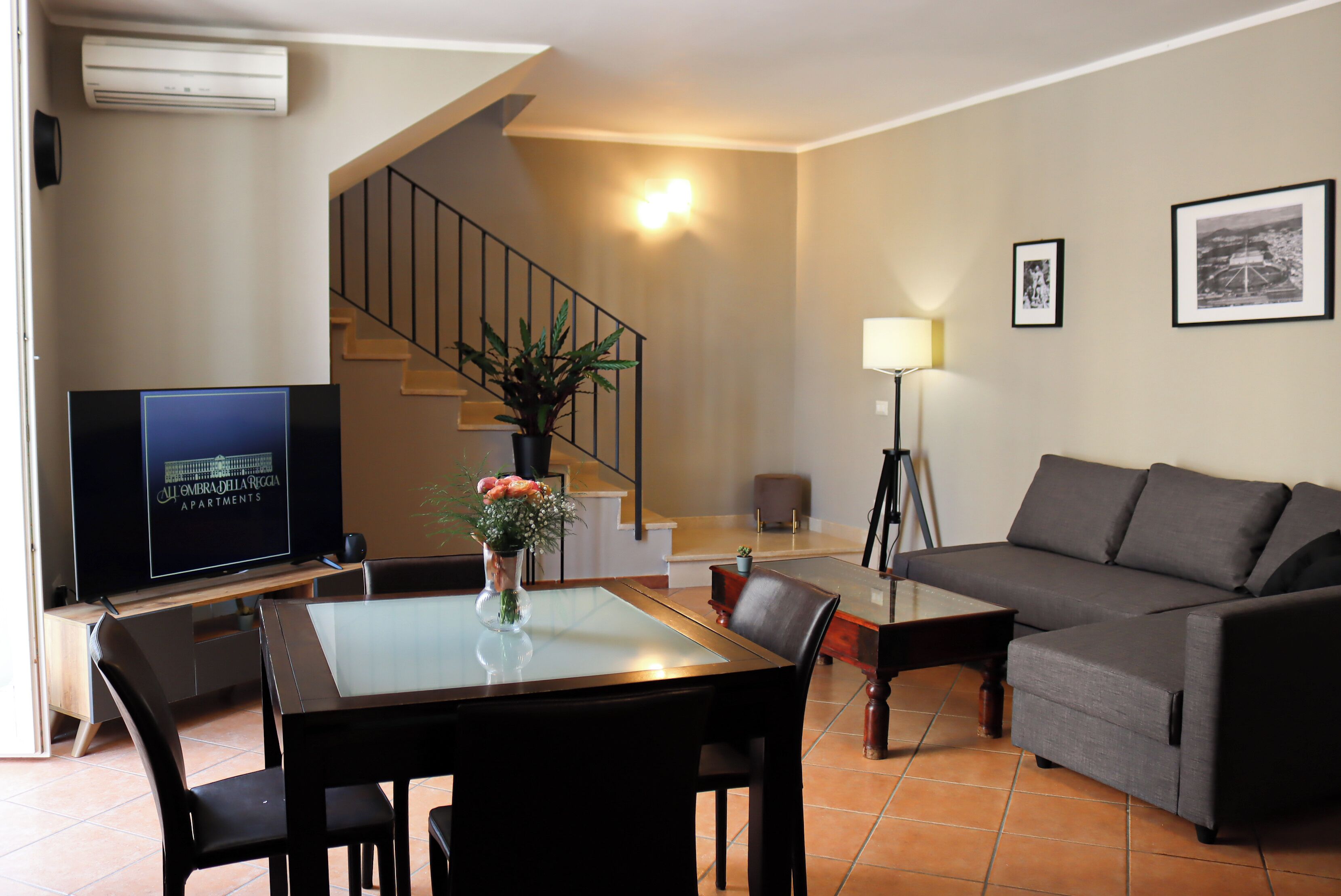 Un soggiorno con divano, TV, tavolo da pranzo, sedie, una scala e una lampada.