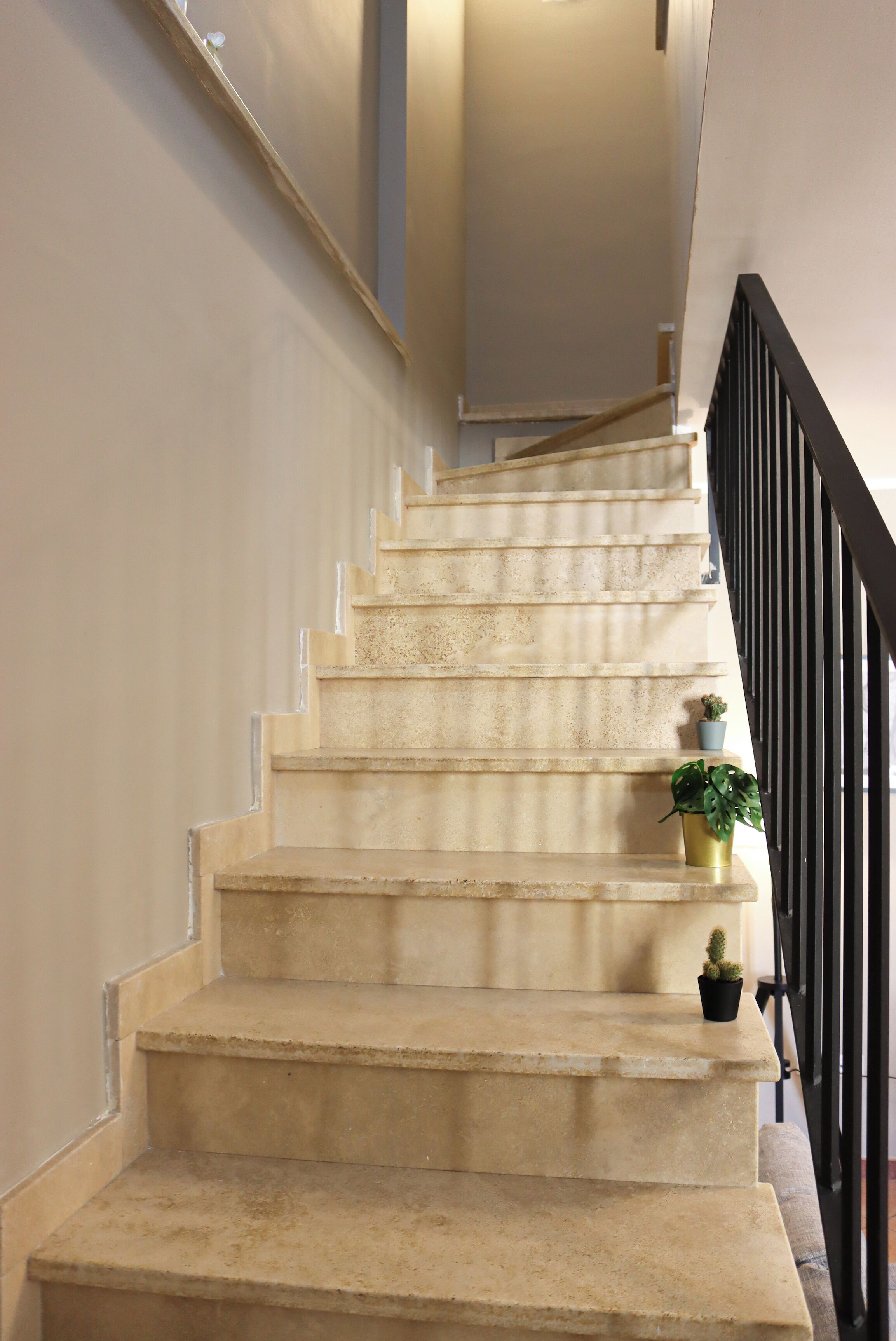 A staircase with beige steps, a black railing, and two potted plants on the landing.