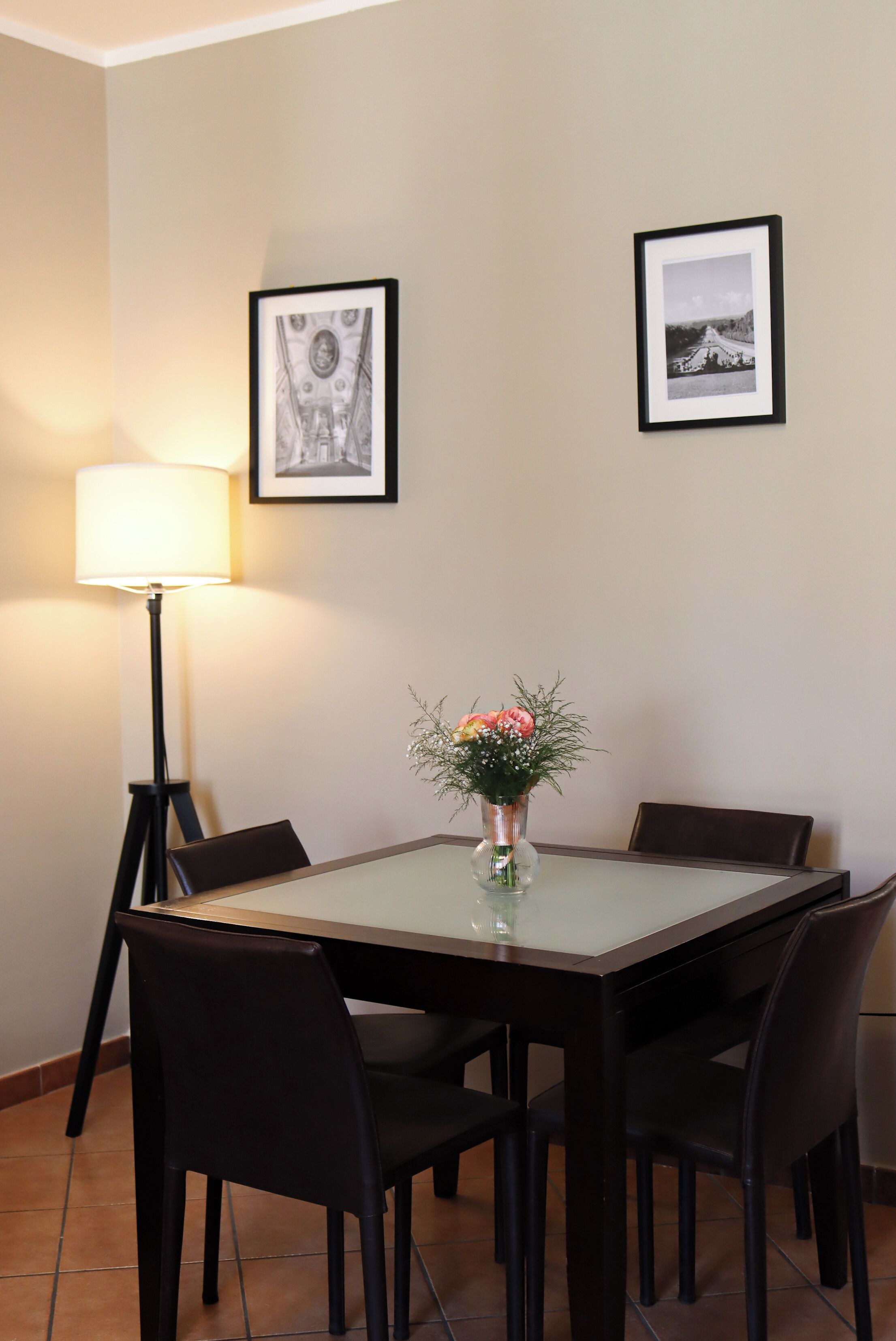 Ein Essbereich mit Tisch, Stühlen, einer Blumenvase, einer Lampe und zwei gerahmten Bildern an der Wand.