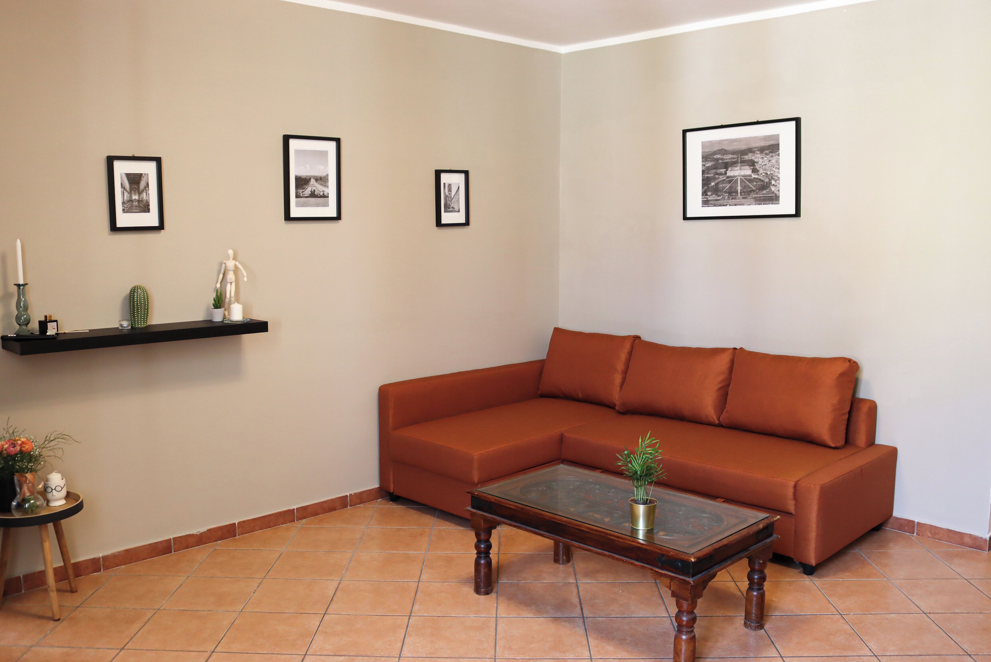 Un salón con un sofá marrón, una mesita de centro y un estante de pared con marcos de fotos y objetos decorativos.