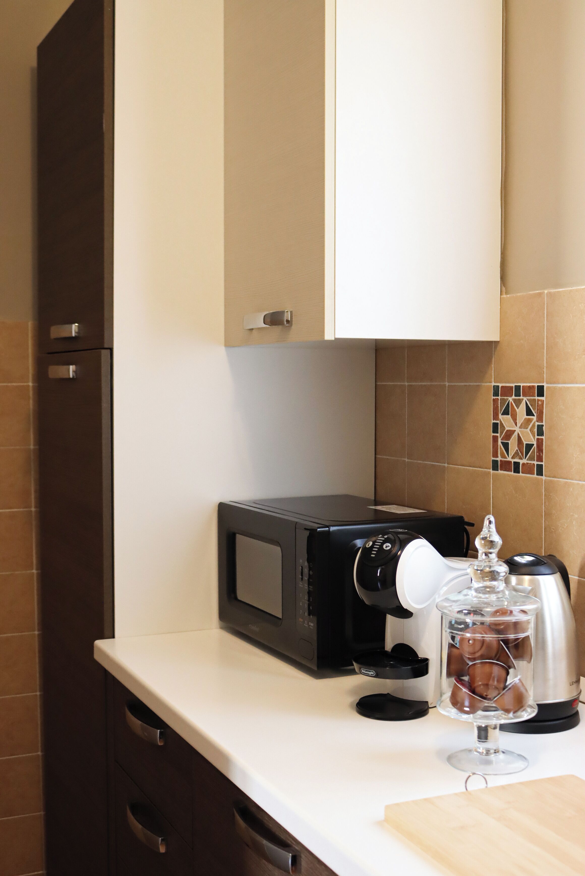 Una cucina con un forno a microonde, una macchina da caffè e un contenitore di vetro sul ripiano.