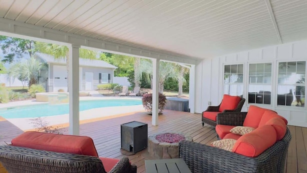 A covered outdoor area with wicker furniture, a pool, and a view of a house and greenery.