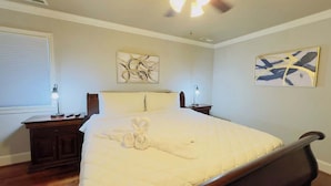 A bedroom with a large bed, two bedside tables, a ceiling fan, and artwork on the walls.