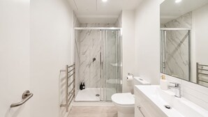 A modern bathroom with a glass-enclosed shower, a toilet, and a vanity with a mirror.
