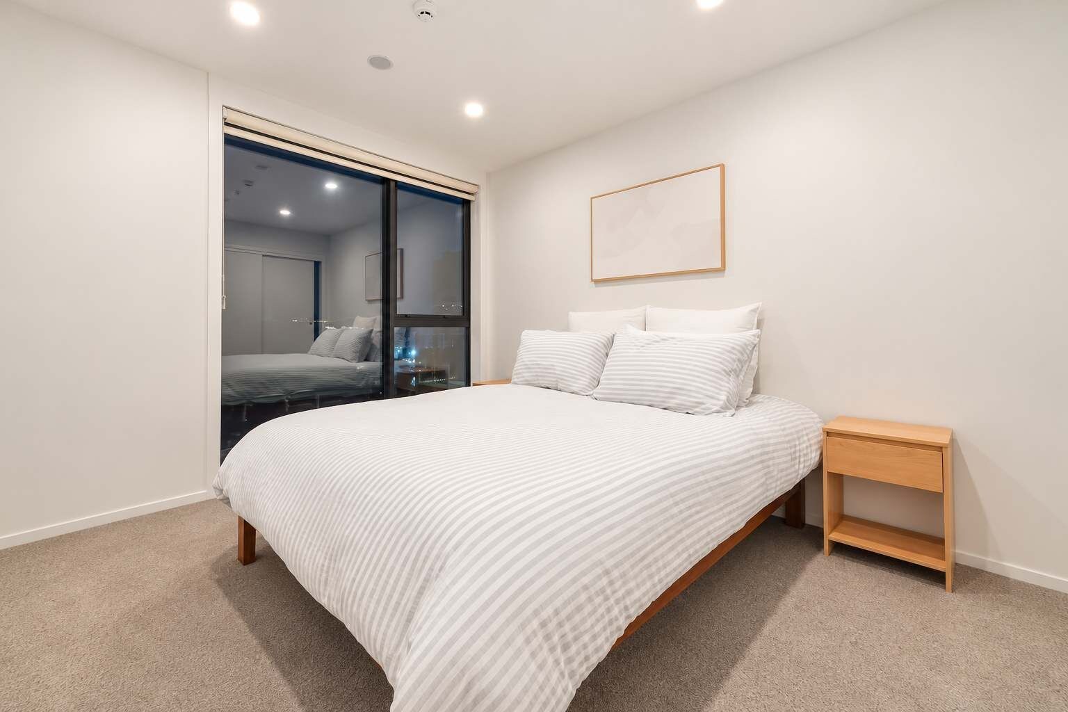 Un dormitorio con cama, mesita de noche, espejo y puerta que da a otra habitación.