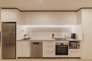 A modern kitchen with stainless steel appliances, white cabinetry, and a tiled backsplash.
