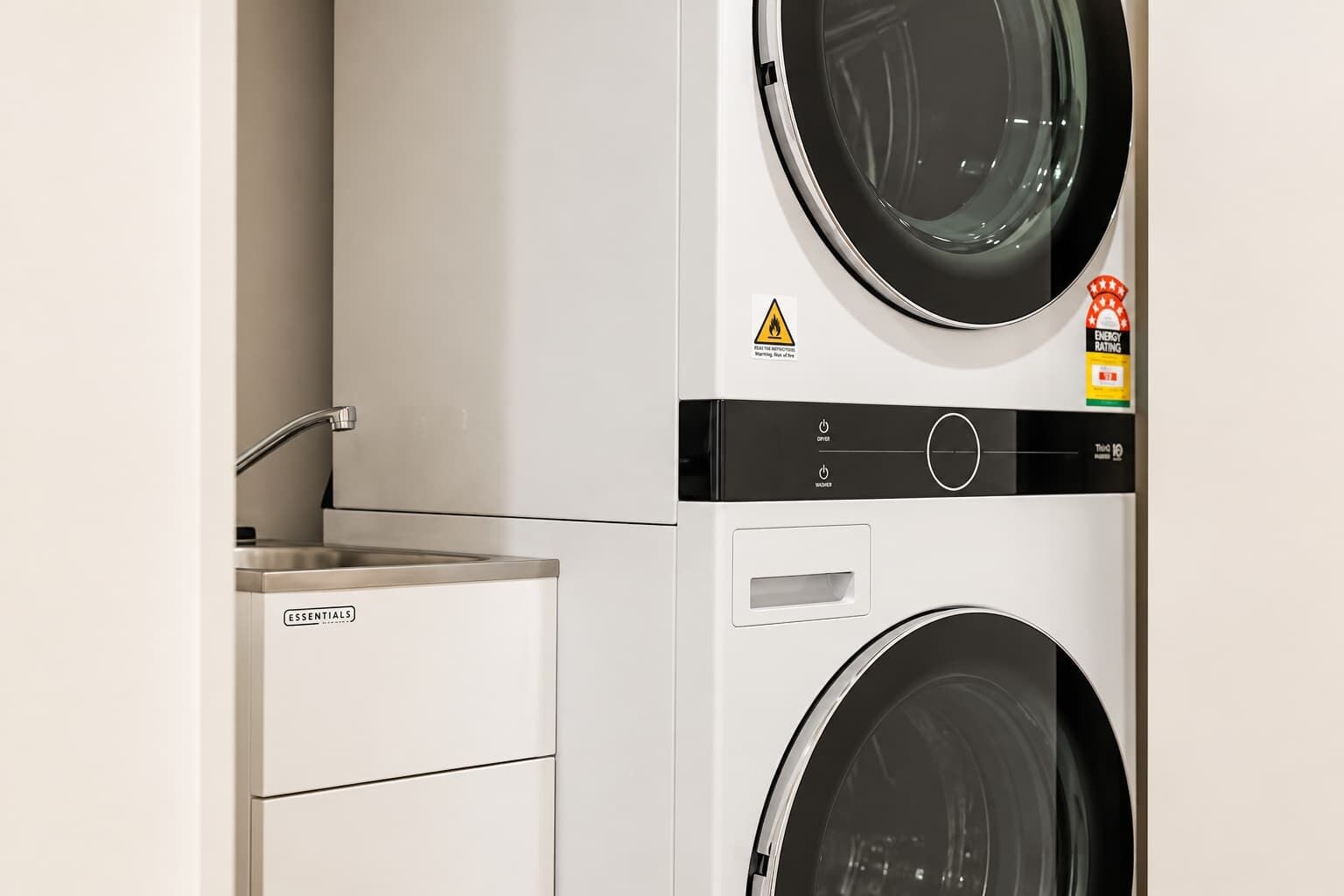 A compact washer and dryer unit with a control panel, a sink, and a caution label.