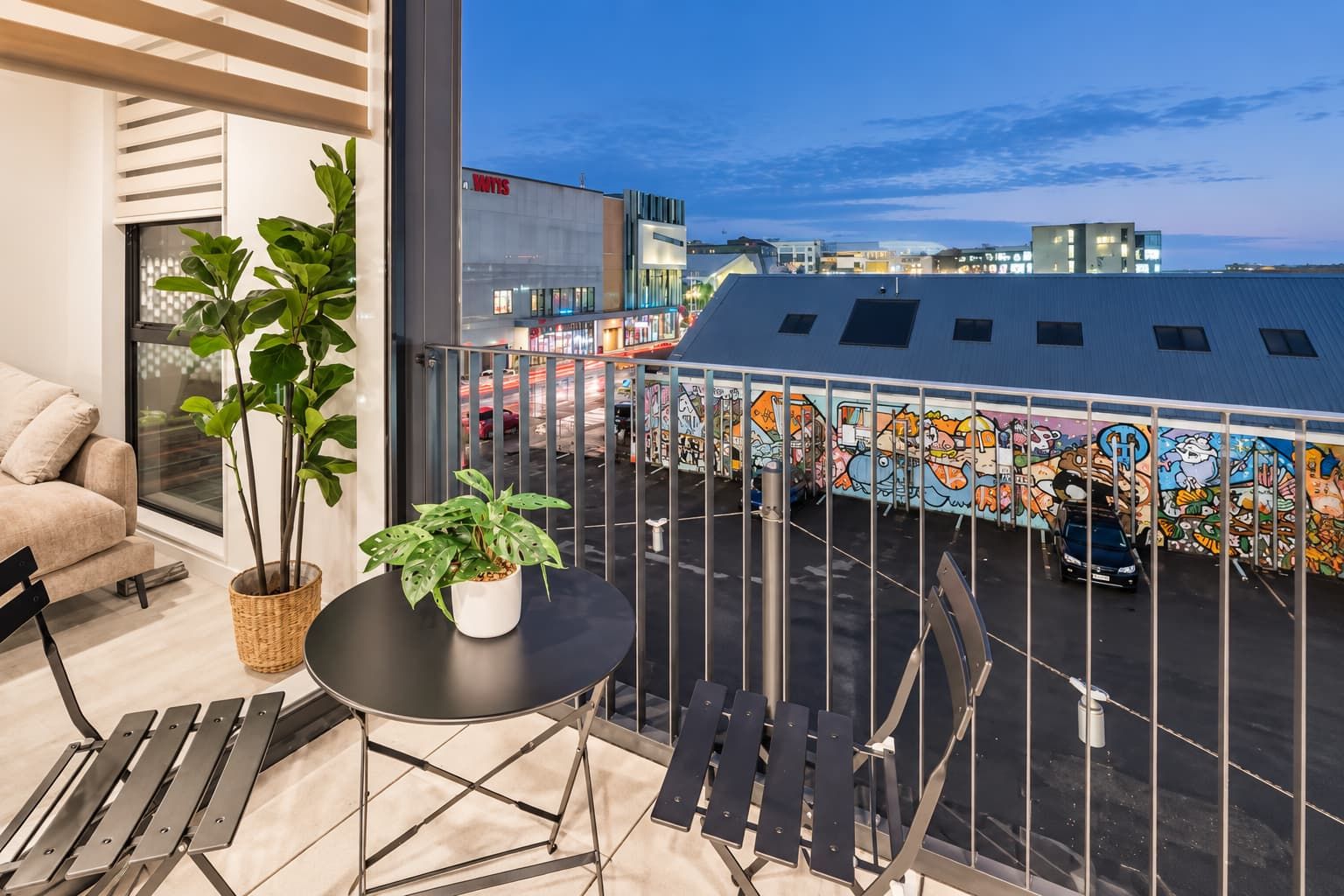 Ein Balkon mit Blick auf eine Stadtlandschaft, einem Blumentopf und einem Tisch mit Stühlen.
