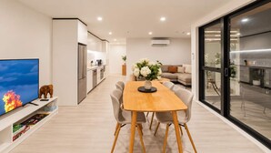 A modern living space with a dining area, kitchen, and a TV on the left.