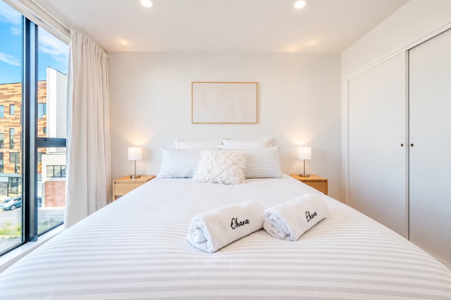 Habitación de hotel con una cama grande, dos lámparas de noche, un cuadro en la pared y vistas al exterior.