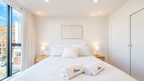 A hotel room with a large bed, two bedside lamps, a framed picture on the wall, and a view of the outside.