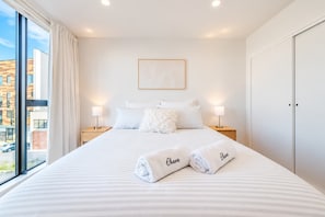 Habitación de hotel con una cama grande, dos lámparas de noche, un cuadro en la pared y vistas al exterior.