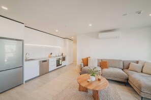 A modern living space with a kitchen, a sofa set, and a round wooden coffee table.