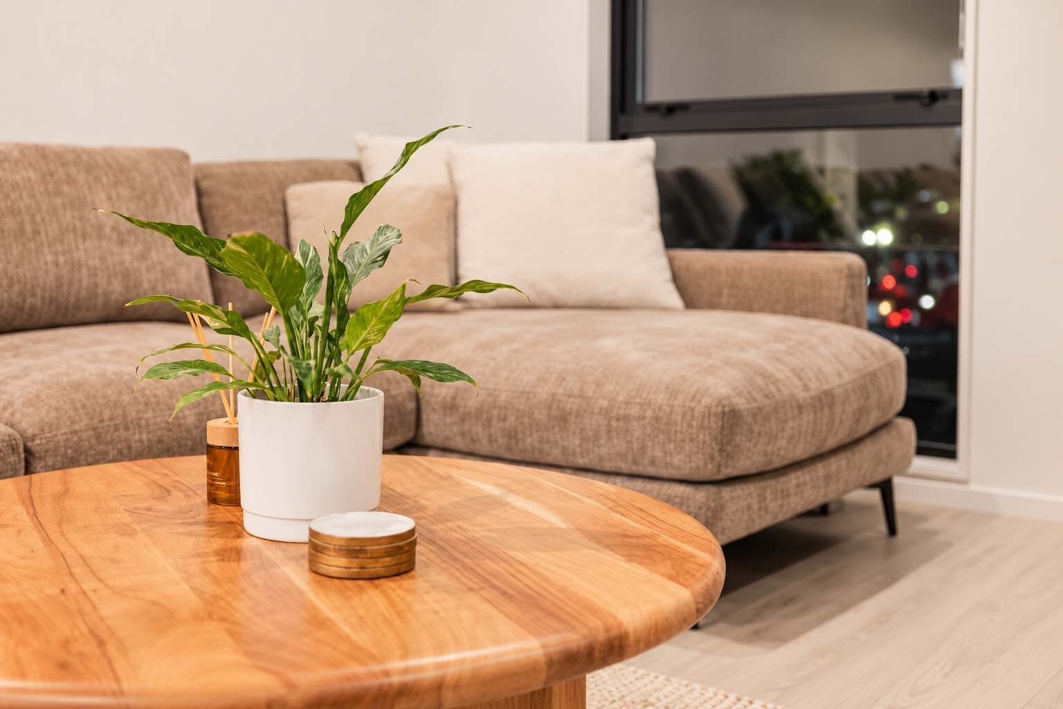 Una sala moderna con una mesa de centro de madera, una planta en maceta y un sofá color beige.
