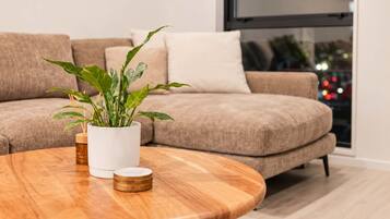 Una sala moderna con una mesa de centro de madera, una planta en maceta y un sofá color beige.