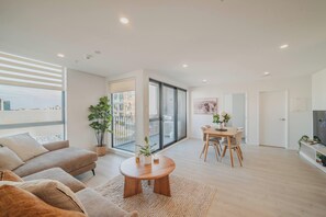 A modern living room with a sofa, a round wooden coffee table, and a dining area with a table and chairs.