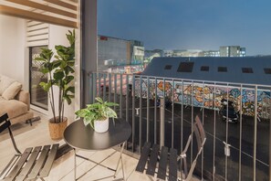A balcony with a potted plant, a small table, and a view of a cityscape with buildings and graffiti.
