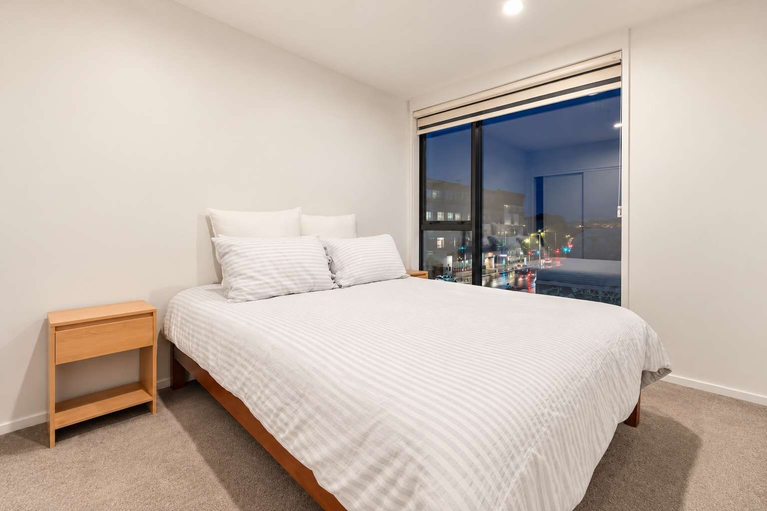 Un dormitorio con cama, mesita de noche y un ventanal con vistas a la ciudad.