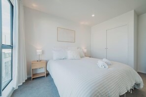 Hotellihuone, jossa on suuri sänky, yöpöytä, sängyn vieressä oleva lamppu, seinällä oleva kehystetty kuva ja ovi.