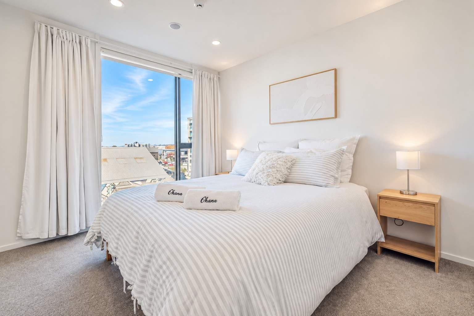 Una habitación de hotel con una cama grande, dos mesitas de noche con lámparas, una ventana con cortinas y un cuadro en la pared.