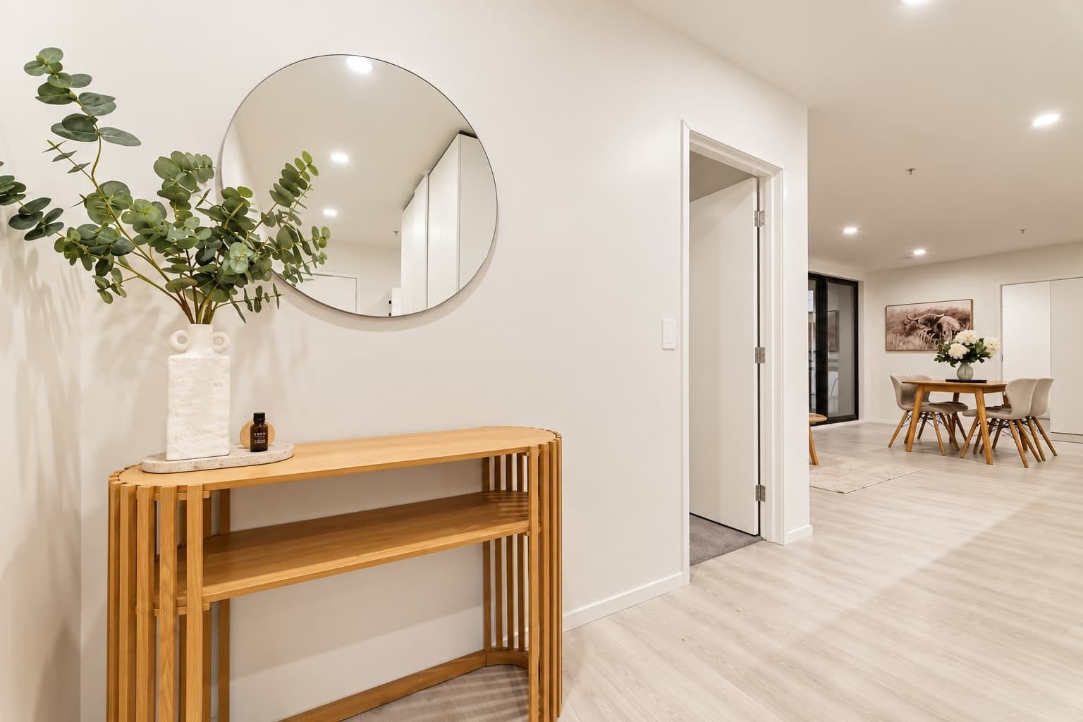 A modern interior with a wooden console table, a round mirror, and a potted plant.