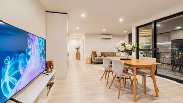 Una sala de estar moderna con un televisor de pantalla plana, un comedor con mesa y sillas de madera, y un sofá con cojines.