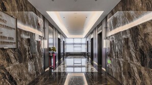 A modern hotel corridor with marble walls and a reflective floor, leading to a bright, well-lit lobby area. - KEEJOY HOTEL (Fuzhou)