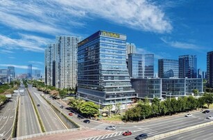 Un moderno edificio de gran altura con varios pisos, rodeado de otros edificios altos, y una transitada avenida de múltiples carriles en primer plano.