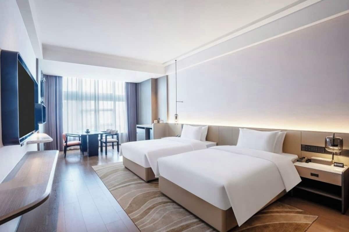 Habitación de hotel con dos camas, un escritorio, televisión y una zona de estar con vistas al exterior.