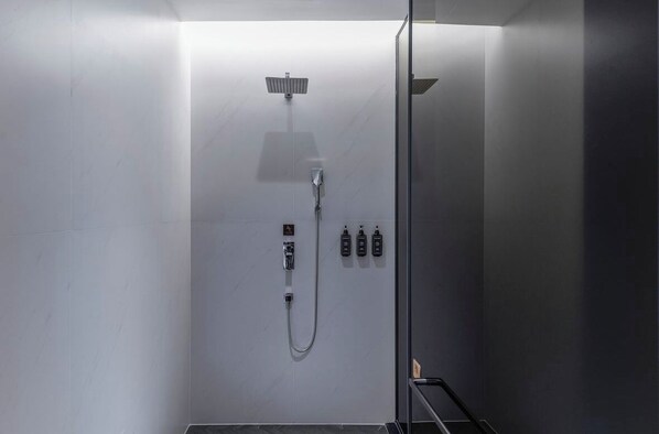 A modern shower with a handheld showerhead, a wall-mounted control panel, and two bottles of shampoo and conditioner.