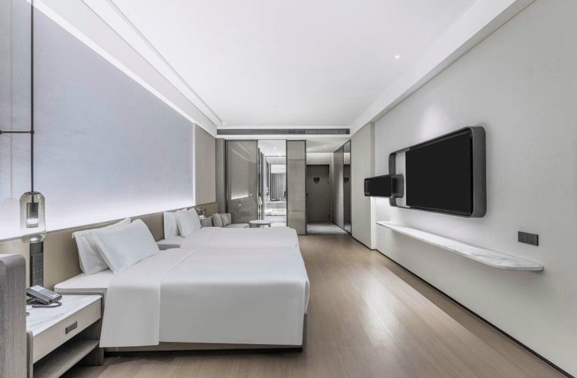 Una habitación de hotel moderna con una cama grande, un televisor montado en la pared y una mesita de noche.