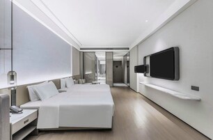 Una habitación de hotel moderna con una cama grande, un televisor montado en la pared y una mesita de noche.