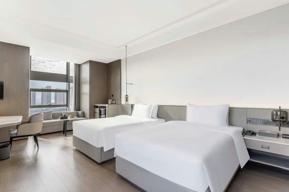 Una habitación de hotel moderna con dos camas, un escritorio, una silla y un ventanal con vistas a la ciudad.