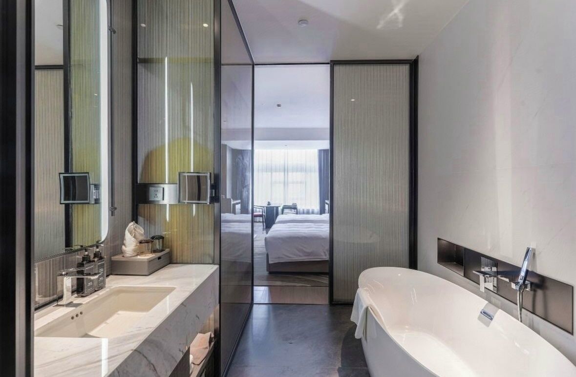 A modern hotel bathroom with a large bathtub, two sinks, and a large mirror.