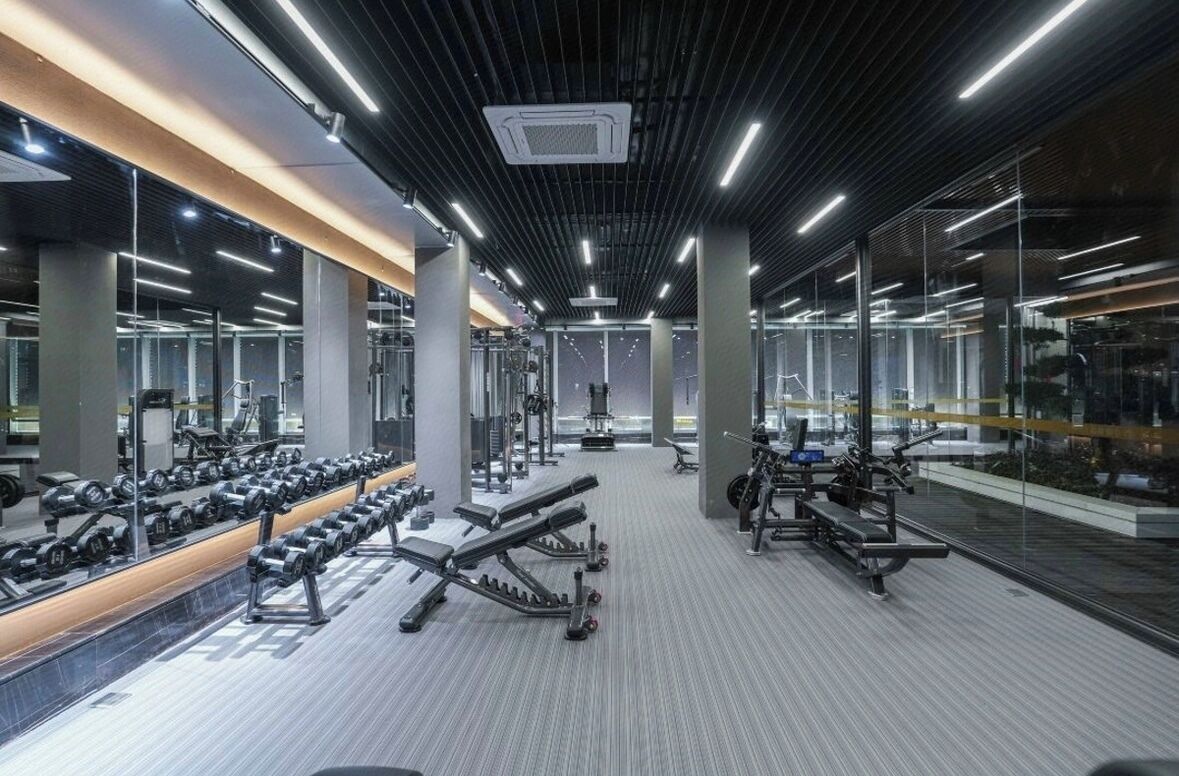 Une salle de sport moderne avec des murs recouverts de miroirs, divers appareils d’exercice et un intérieur propre et bien éclairé.