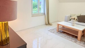 A modern living room with a large window, a sofa, a coffee table, and a lamp. - Luxrem 5 Apartments Skyline (Biel)