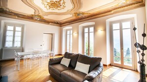 Un salon spacieux avec un canapé en cuir marron, une table à manger blanche avec des chaises, de grandes fenêtres et un plafond décoratif.