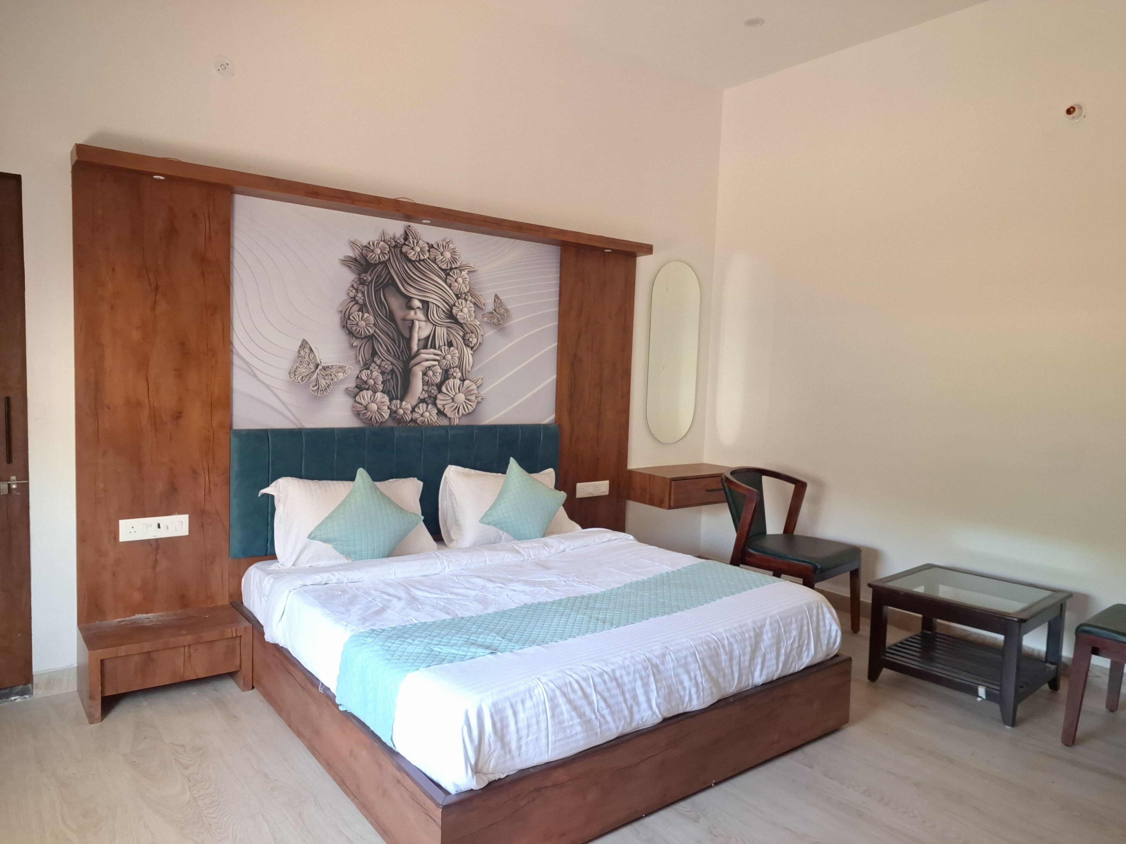 A bedroom with a wooden headboard, a large wall art piece, a bedside table, a chair, and a small table.