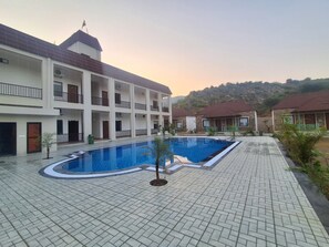 A swimming pool surrounded by a tiled courtyard with a building featuring balconies and a mountain backdrop. - Orchard Hills Resorts (Pushkar)