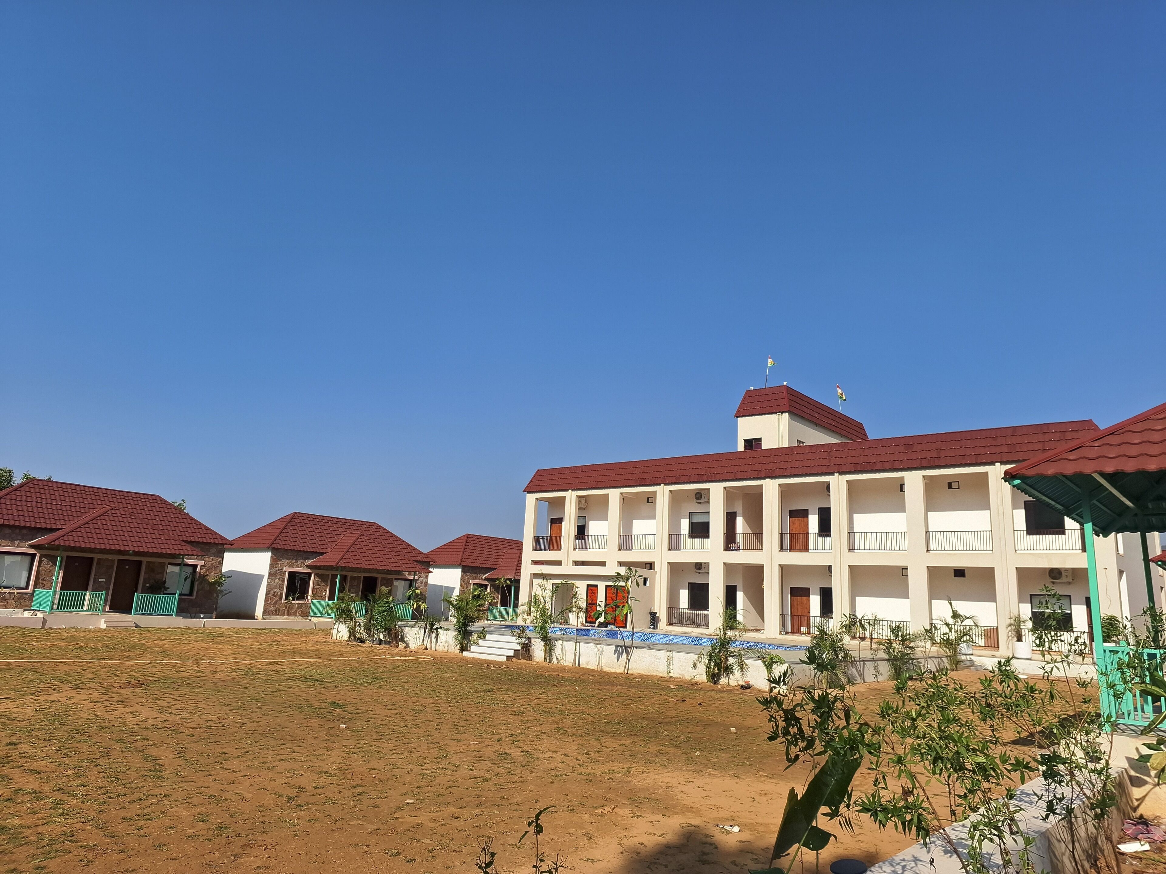 A multi-story building with a red roof, surrounded by a grassy area and smaller structures with similar roofs.