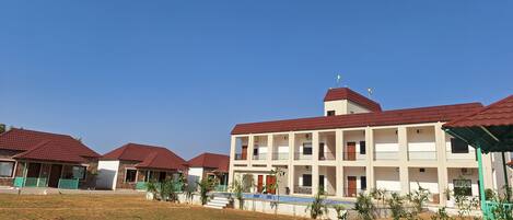 A multi-story building with a red roof, surrounded by a grassy area and smaller structures with similar roofs.