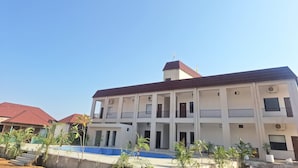 A multi-story building with balconies, a swimming pool, and a red-roofed structure in the background. - Orchard Hills Resorts (Pushkar)
