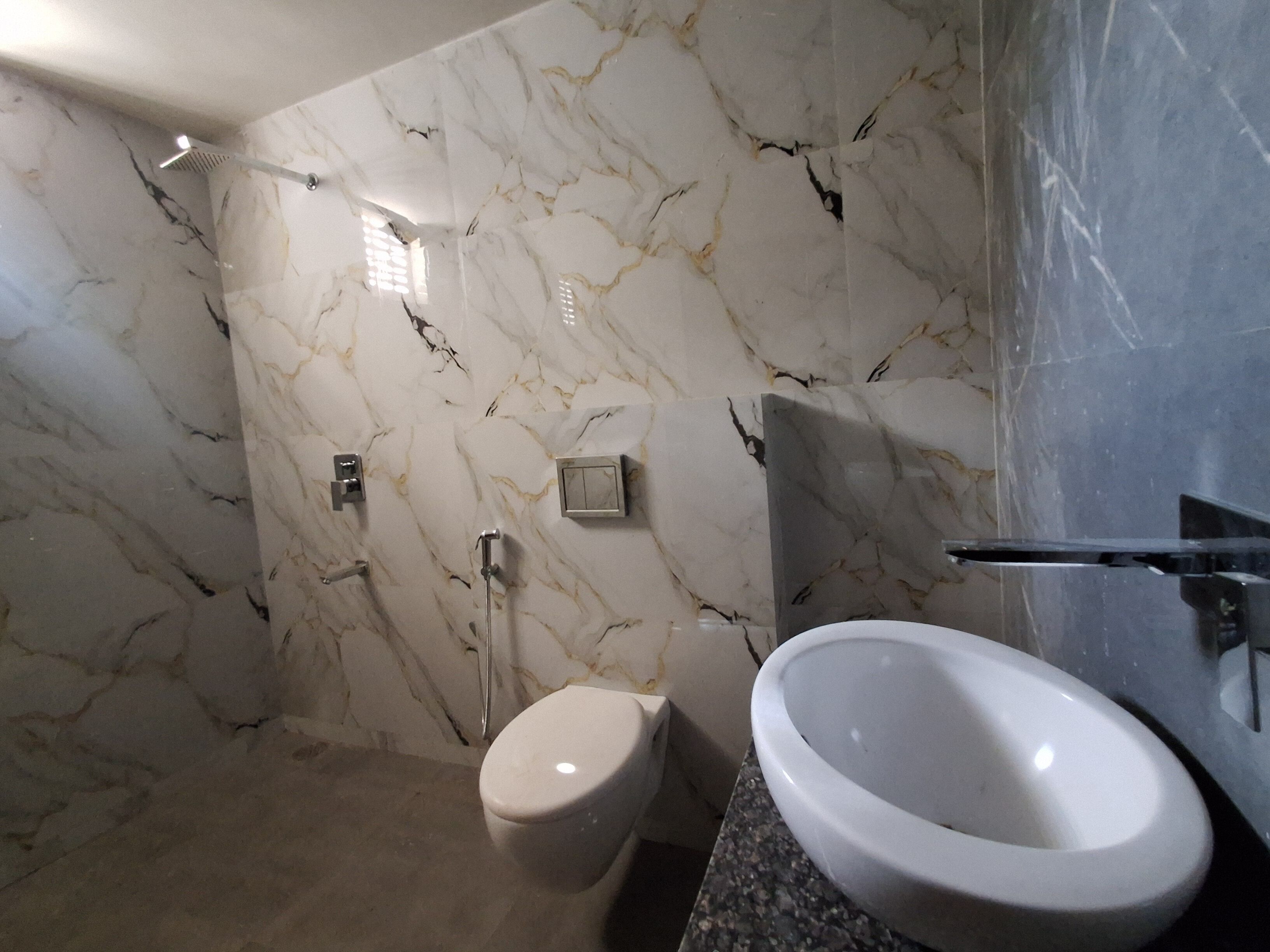 A bathroom with a marble wall, a white toilet, a sink, and a shower.