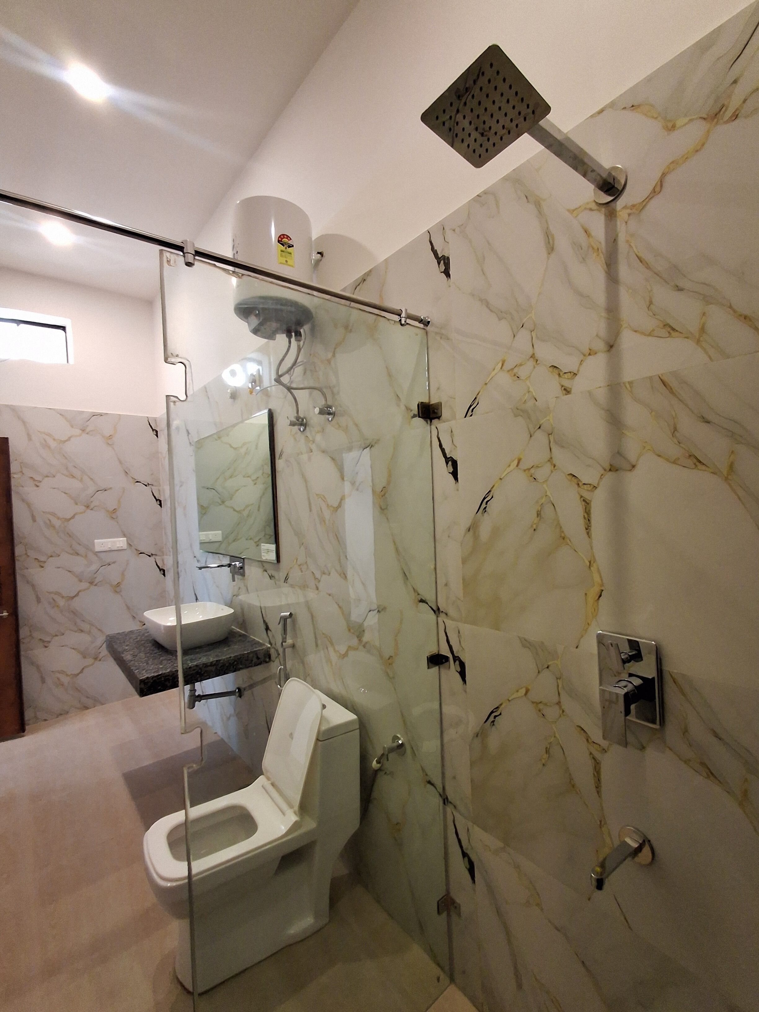 A modern bathroom with a glass-enclosed shower, a marble wall, a sink, and a toilet.