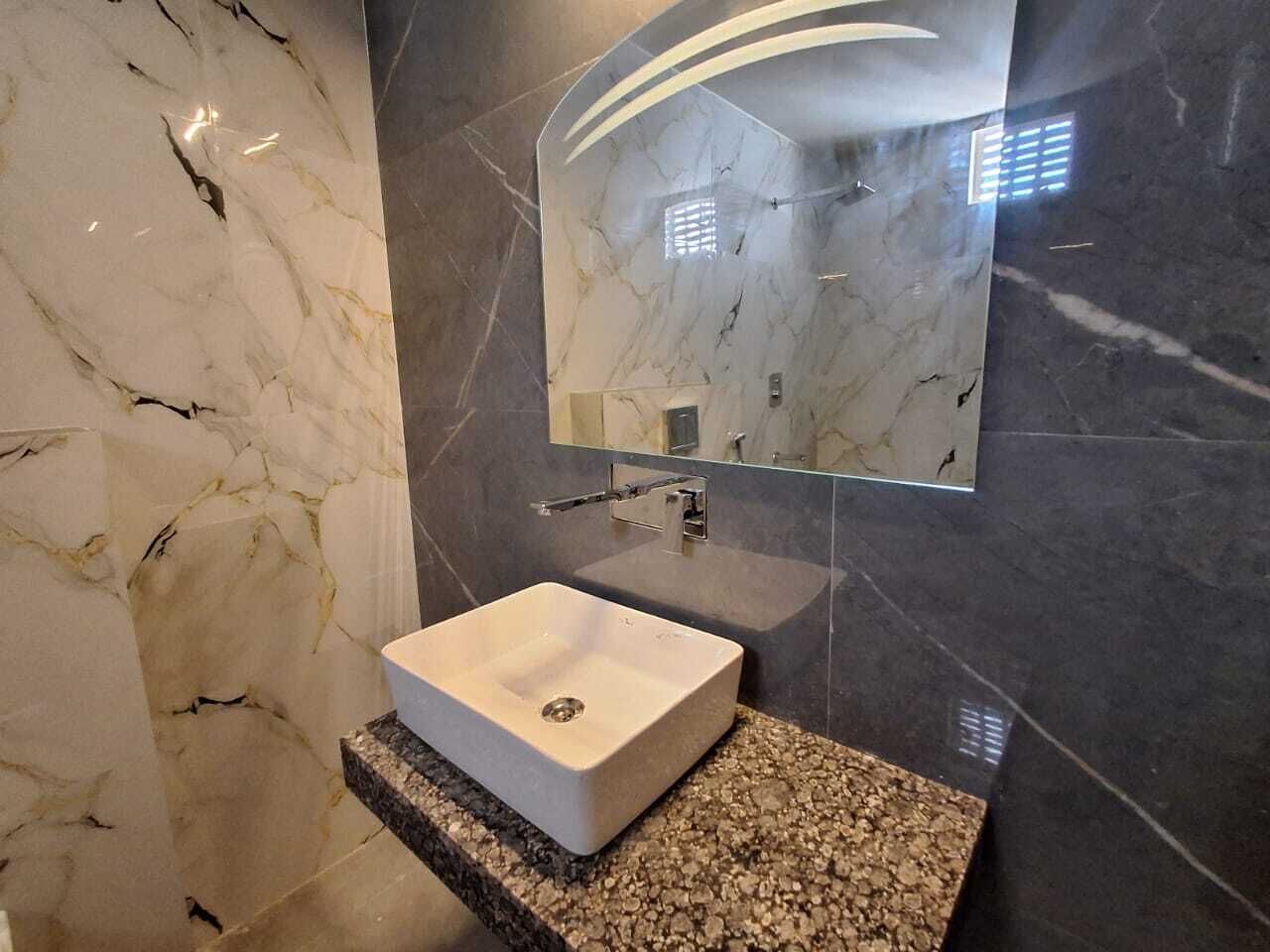 Une salle de bain avec un lavabo en marbre blanc, un plan de travail en granit et un miroir doté d’un cadre incurvé.