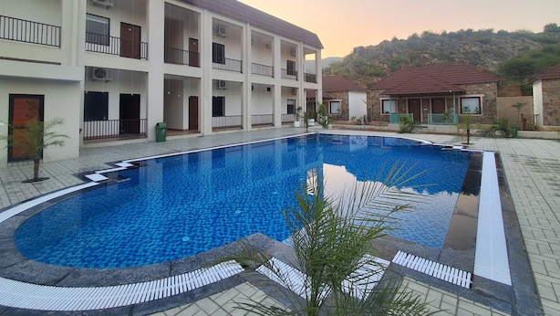 A swimming pool surrounded by a multi-story building with balconies and air conditioning units. - Orchard Hills Resorts (Pushkar)